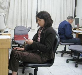 '唐慧如（左）正在给中国大陆民众拨打电话，八十多岁的老学员（右）正在告诉大陆民众三退的讯息。'