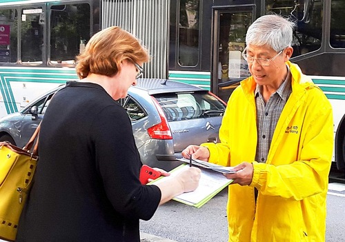 Sarah Nimoelc, sedang menunggu bis di depan spanduk, ia mendukung Falun Gong dan menandatangani petisi untuk menentang penganiayaan / penyiksaan