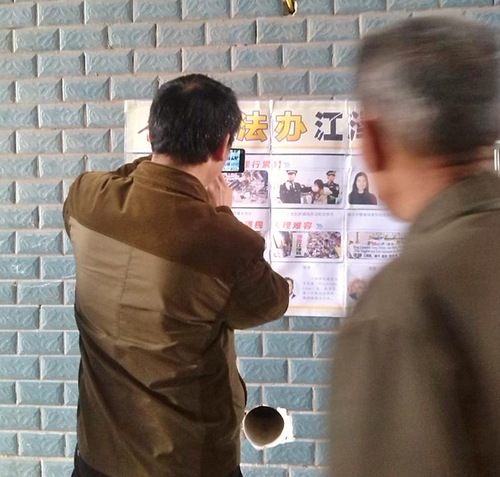 Seseorang membaca poster di Kota Nanchong di Provinsi Sichuan di Tiongkok tengah, sementara yang lain mengambil gambar.