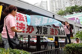 穿着粉红色制服的“香港青年关爱协会”中共帮凶，用带来的横幅掩盖法轮功学员的横幅，故意挑衅香港法轮功学员。