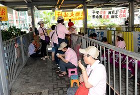 十多名身穿粉红色统一制服，上印香港青年关爱协会的帮凶，十九日冲进法轮功学员真相点内，四处悬挂污蔑横幅，又大摇大摆吃东西，用尽各种方法挑衅。